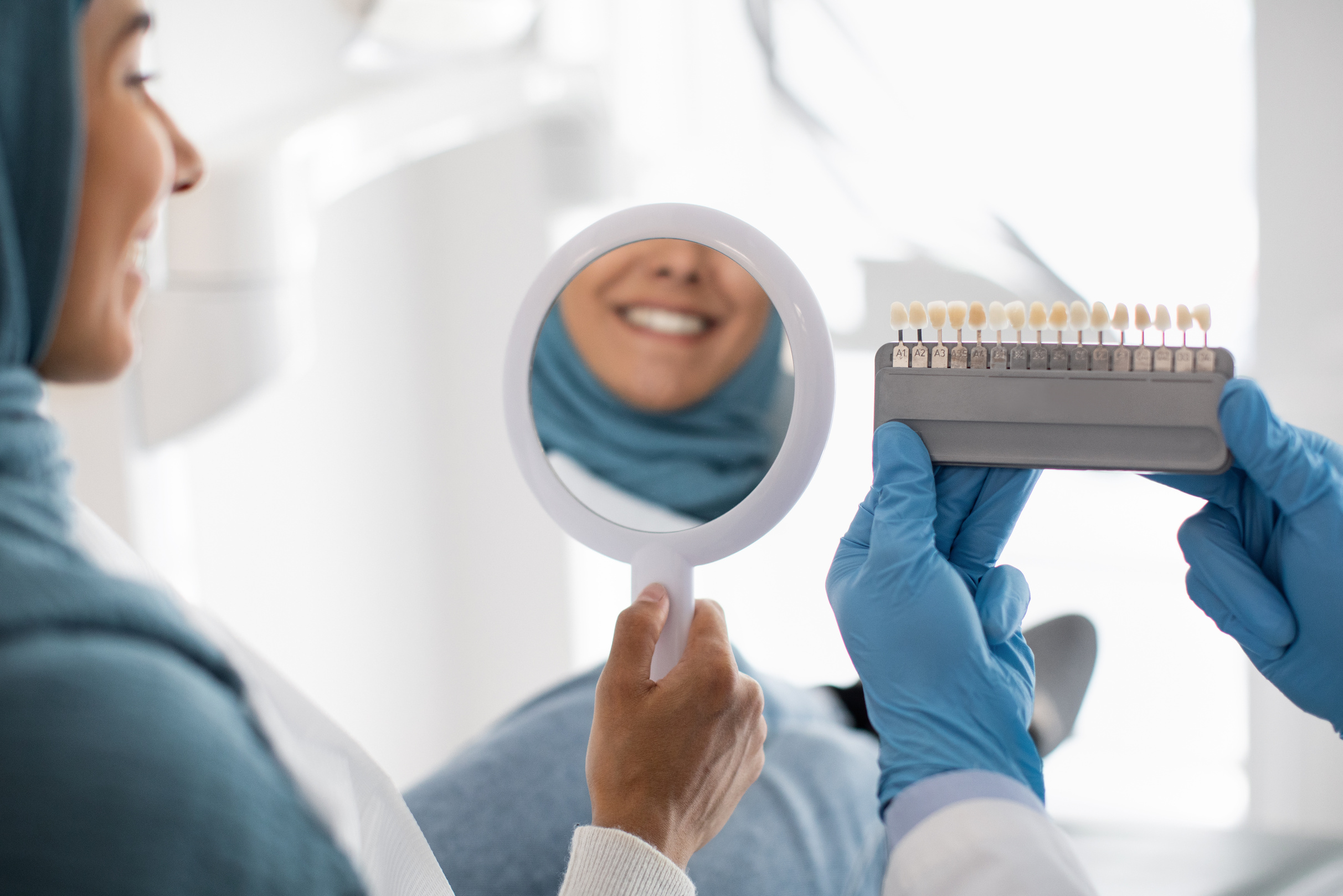 Restorative Dentistry. Muslim Female Patient Holding Mirror and Looking at Her Smile